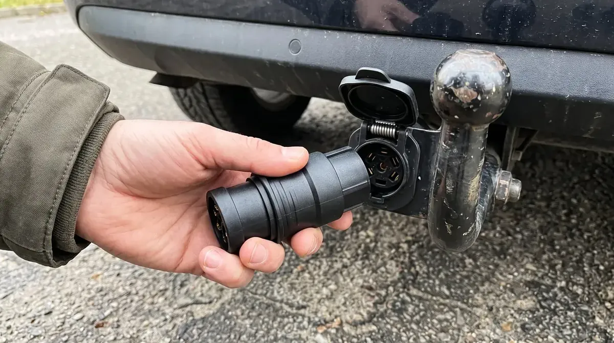 Adapter 13/7 pin trzymany w dłoni przy gnieździe elektrycznym haka holowniczego samochodu