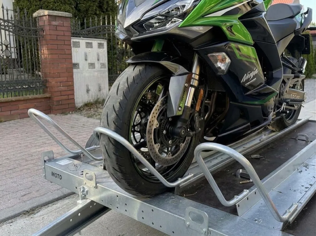 Przednie koło motocykla Kawasaki Ninja zablokowane w kołysce przyczepki – motocykl stoi pionowo bez bocznej stopki