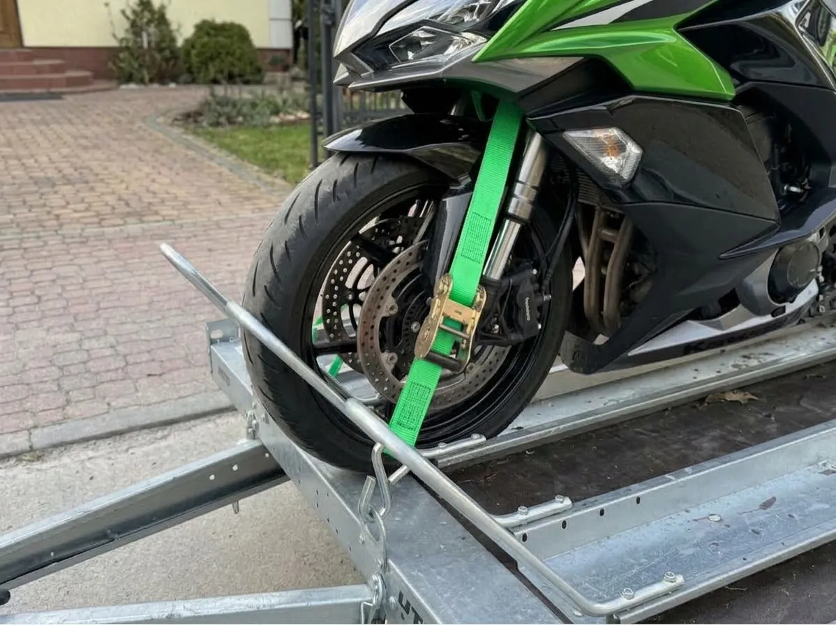 Przedni pas z napinaczem zaczepiony przy zawieszeniu motocykla i uchwycie przyczepy, przednie koło w kołysce