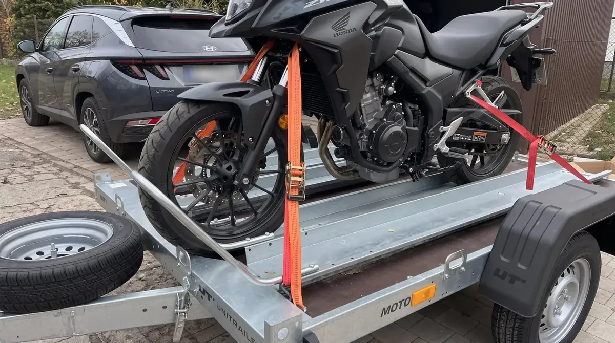 Motocykl Honda spięty pasami z napinaczami, przednie koło w kołysce przyczepki motocyklowej